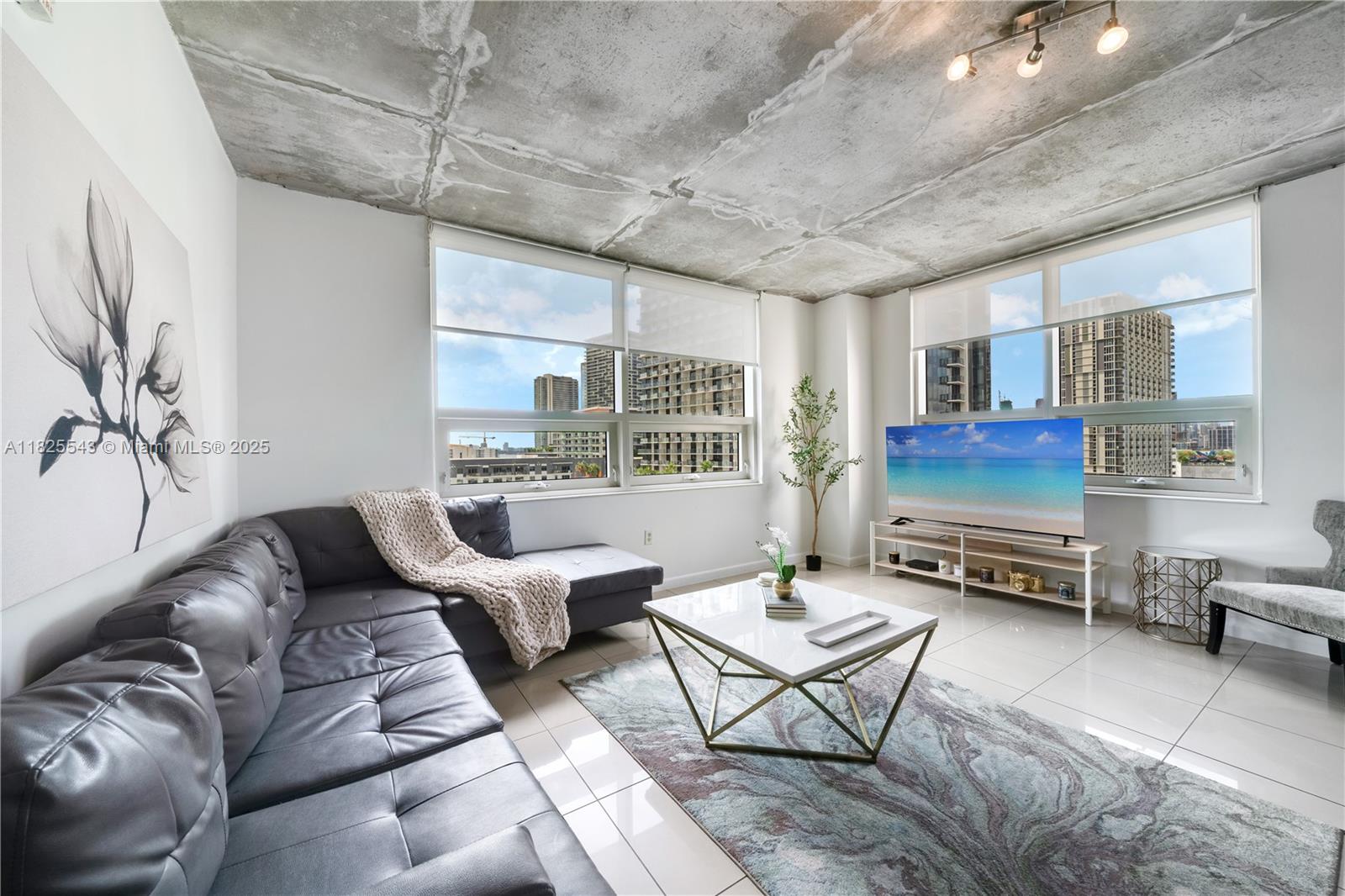 A modern living room features a grey sectional sofa, white coffee table, and exposed concrete ceiling — 3250 NE 1st Ave # 1016, Miami FL 33137, MIAMI, FL