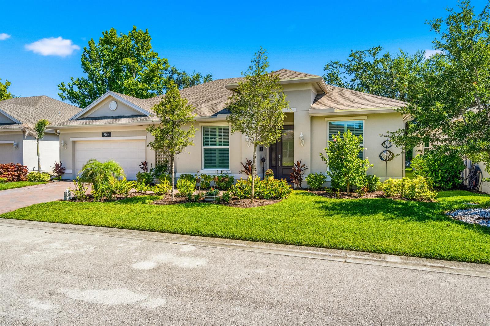A single-story suburban house with a beige stucco exterior, a two-car garage, and landscaped lawn — 6012 Bella Rosa Lane, Vero Beach FL 32966, VERO BEACH, FL