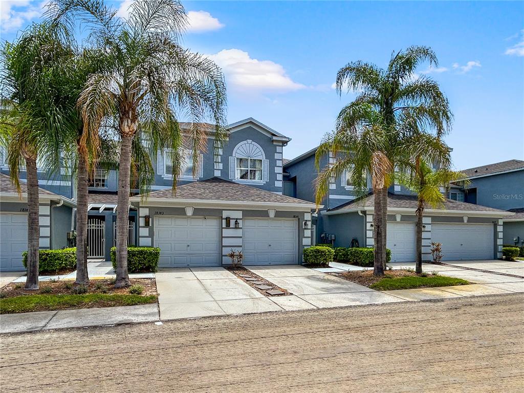 A multi-unit residential building with gray stucco walls, multiple garage doors, and palm trees — 18141 NASSAU POINT DRIVE, TAMPA, FL