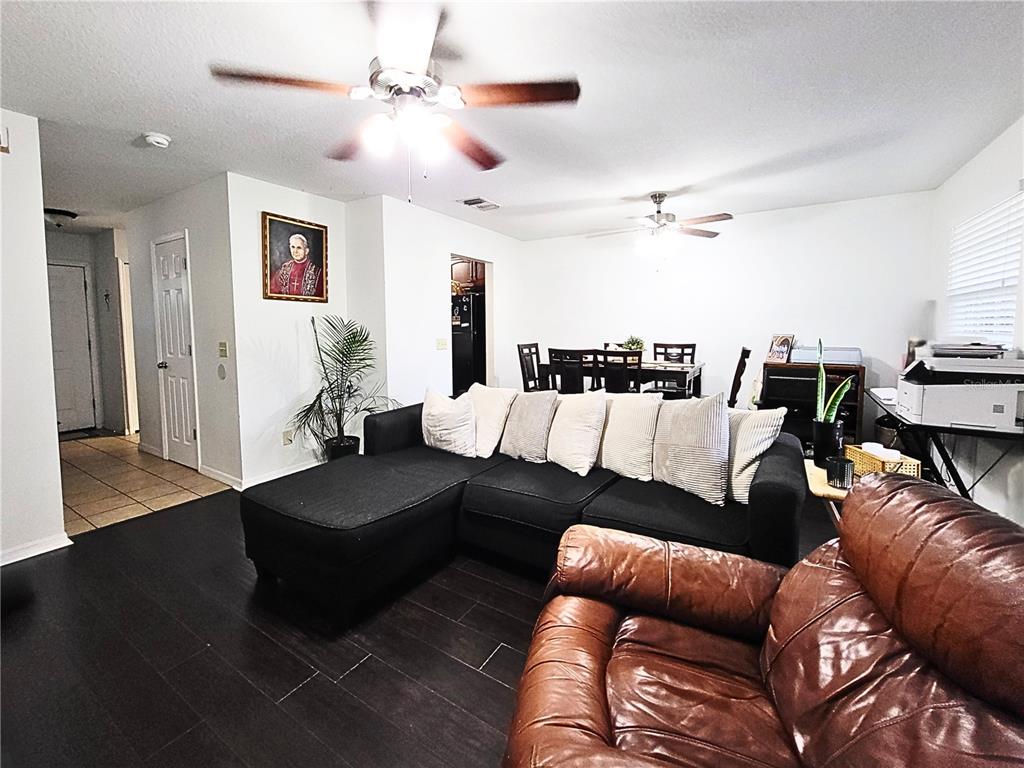 A living room with dark wood floors, a black sectional sofa, and a brown leather chair — 11807 MINTWOOD COURT, ORLANDO, FL