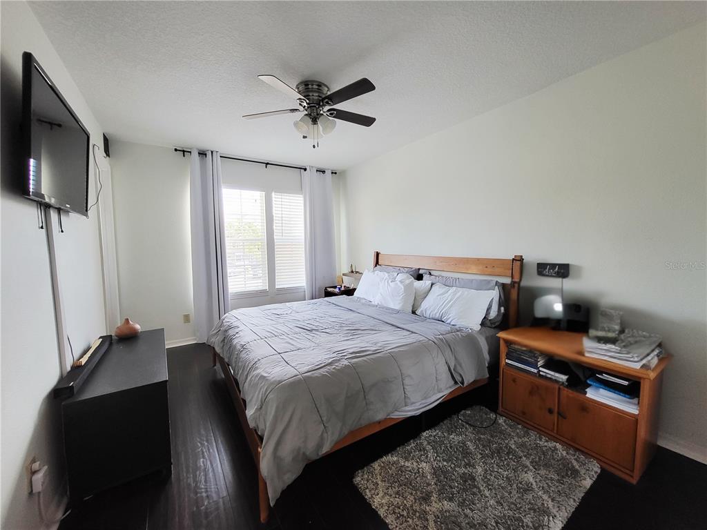 A bedroom features a wooden bed frame, dark flooring, a ceiling fan, and a television — 11807 MINTWOOD COURT, ORLANDO, FL