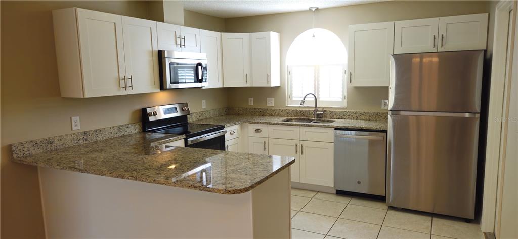A kitchen features white cabinets, granite countertops, stainless steel appliances, and tile flooring — 407 WHITEWING CIRCLE, MINNEOLA, FL