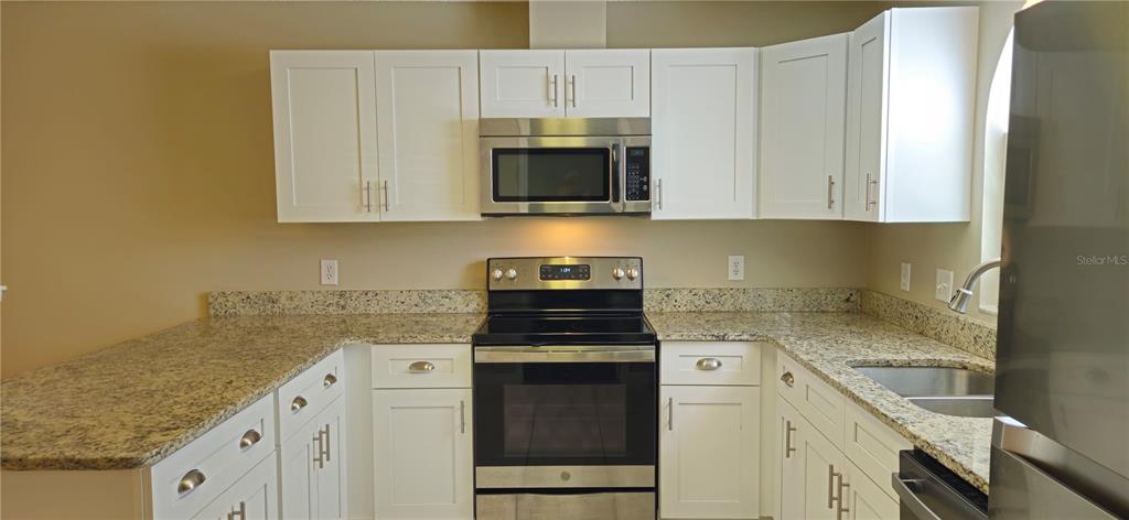 A kitchen features white cabinets, granite countertops, and stainless steel appliances — 407 WHITEWING CIRCLE, MINNEOLA, FL