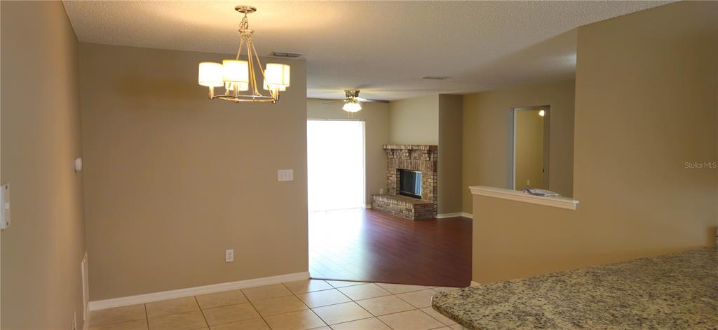 A dining area with a chandelier leads into a living room featuring a brick fireplace — 407 WHITEWING CIRCLE, MINNEOLA, FL