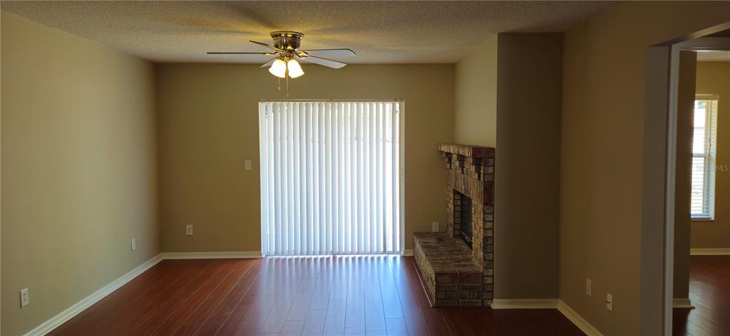 A living room features wood-look flooring, a brick fireplace, and sliding glass doors with blinds — 407 WHITEWING CIRCLE, MINNEOLA, FL