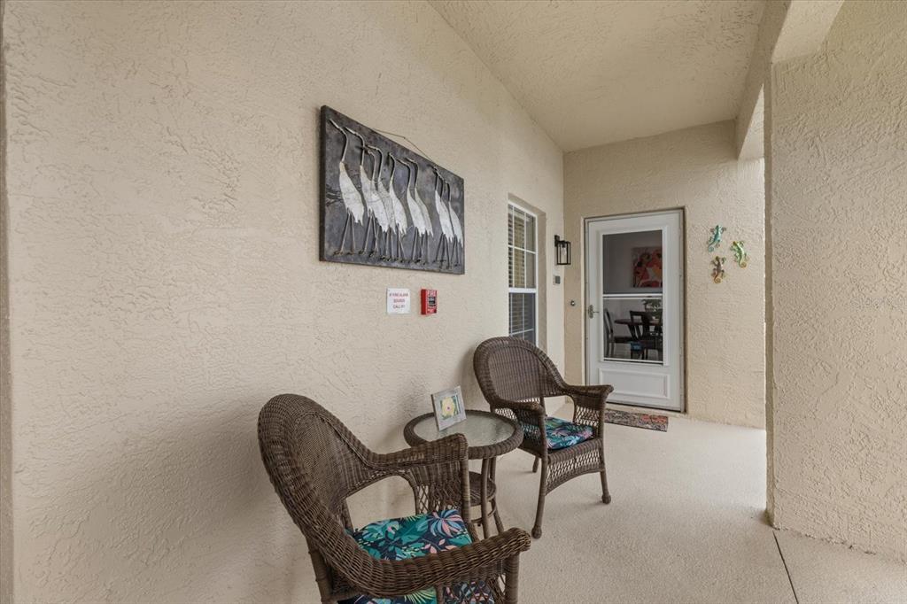 A covered patio features two wicker chairs, a small table, and wall-mounted heron artwork — 5800 SABAL TRACE DRIVE UNIT 103, NORTH PORT, FL