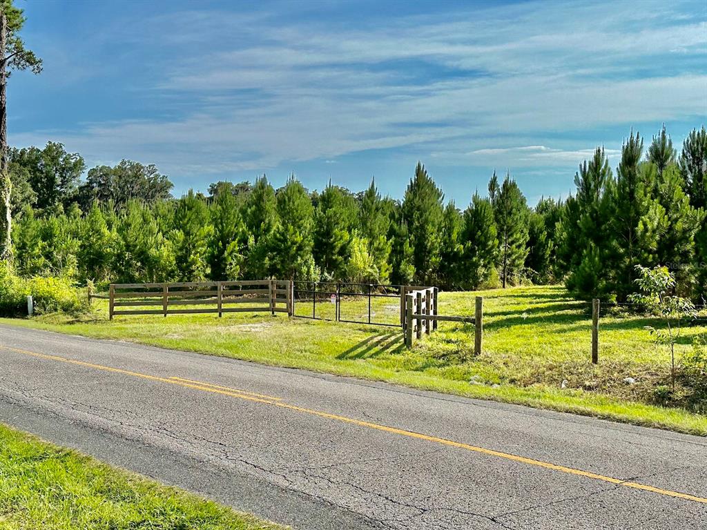 A paved road runs alongside a grassy lot enclosed by a wooden and wire fence — TBD (B, C & D Parcels) NW 160TH AVENUE, MORRISTON, FL