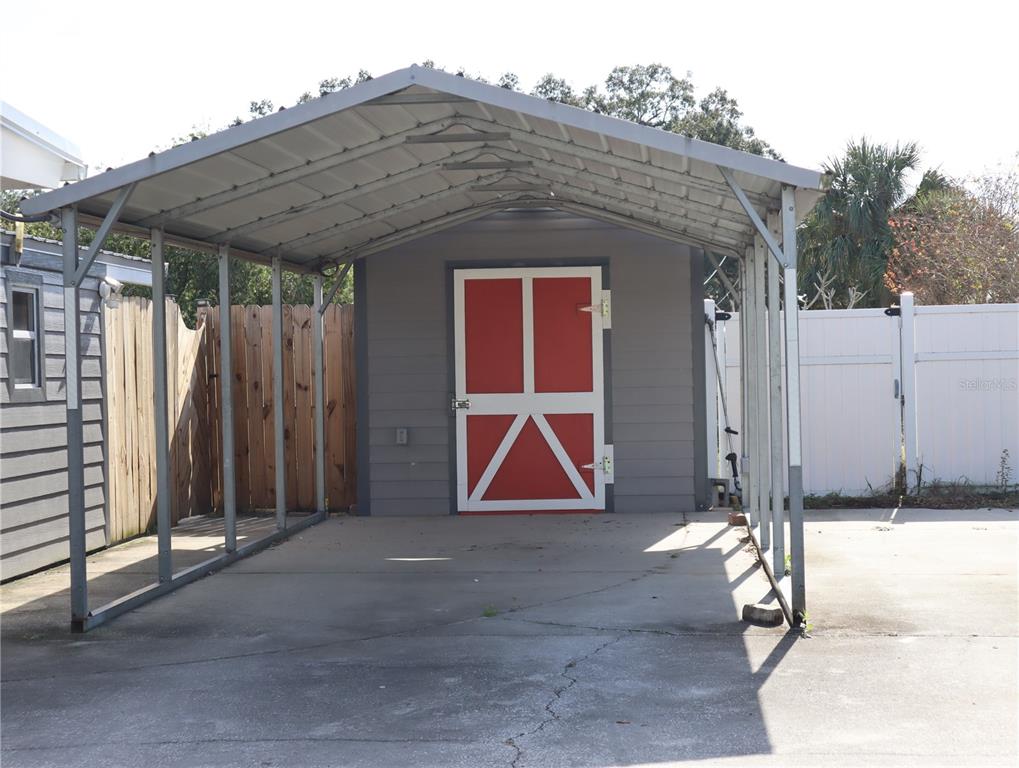 A gray shed with red double doors sits under a metal carport on a concrete pad — 940 OLEANDER DRIVE SE, WINTER HAVEN, FL