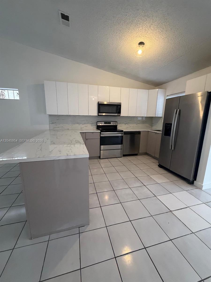 A kitchen features white upper cabinets, gray lower cabinets, stainless steel appliances, and marble-look countertops — 10364 NW 128th Ter, Hialeah Gardens FL 33018, HIALEAH GARDENS, FL