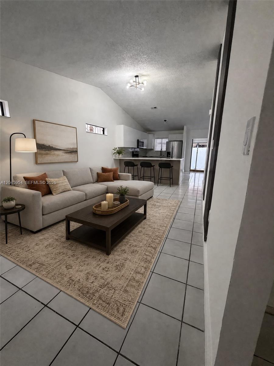 A living room with a sectional sofa and coffee table opens to a kitchen area — 10364 NW 128th Ter, Hialeah Gardens FL 33018, HIALEAH GARDENS, FL