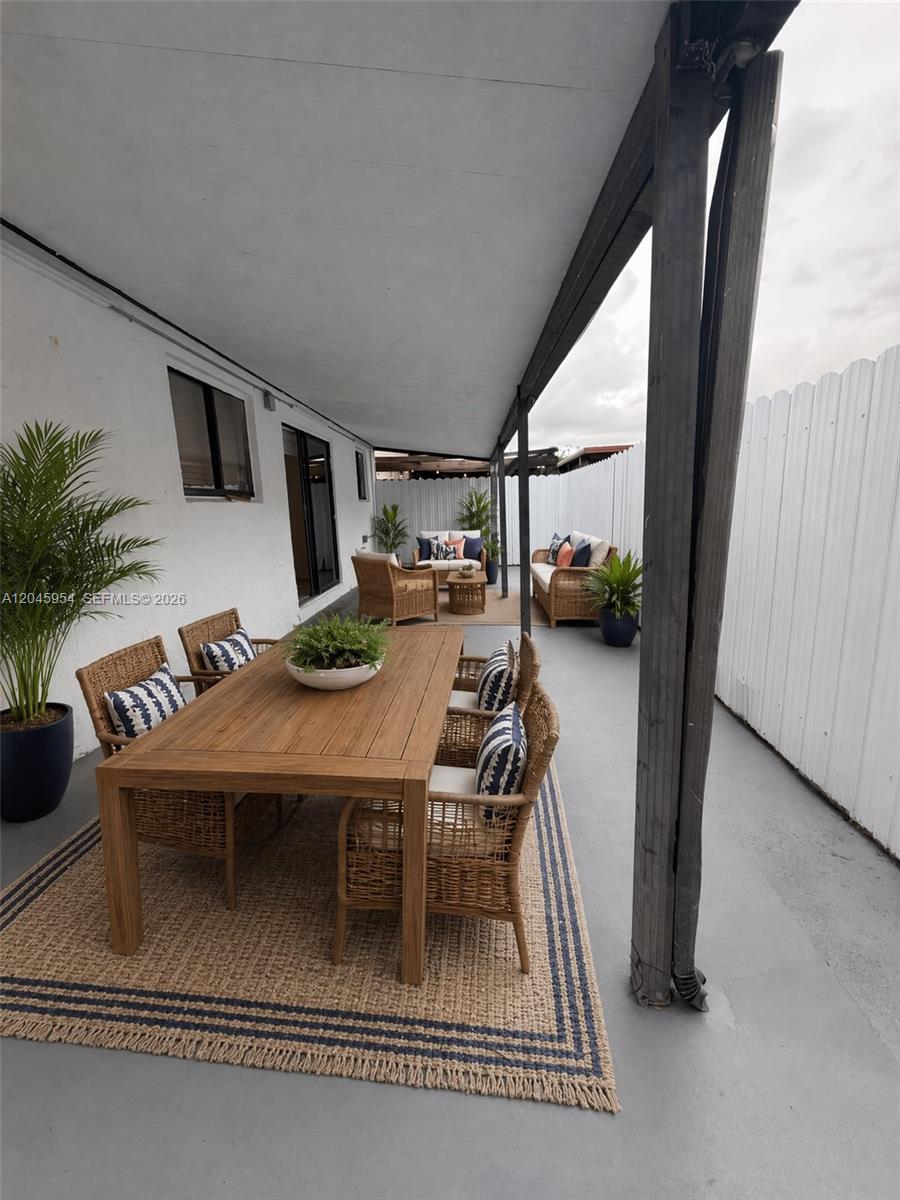 A covered outdoor patio features a wooden dining set and lounge furniture on rugs — 10364 NW 128th Ter, Hialeah Gardens FL 33018, HIALEAH GARDENS, FL