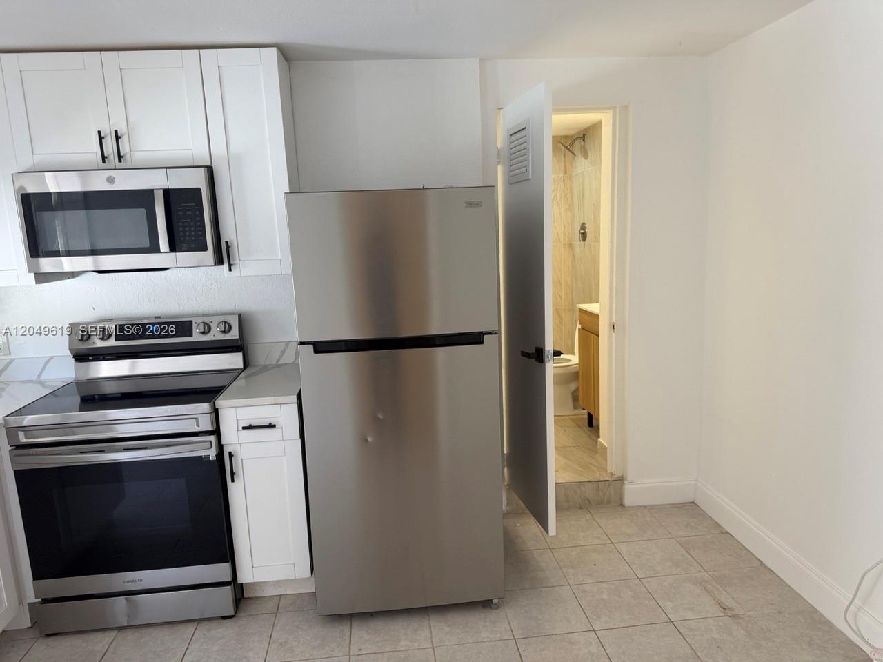 A stainless steel refrigerator and stove are in a kitchen with white cabinets and tile — 219 SW 21st Ave # 5, Miami FL 33135, MIAMI, FL