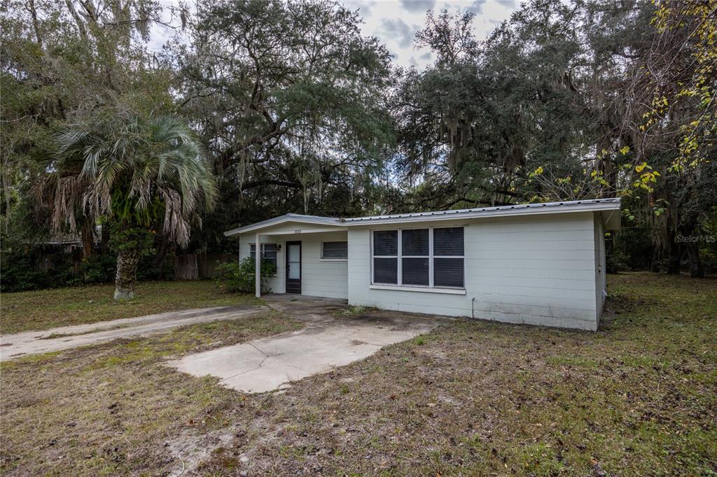 A single-story white house with a metal roof sits on a lot with trees — 1503 SE 28TH PLACE, GAINESVILLE, FL