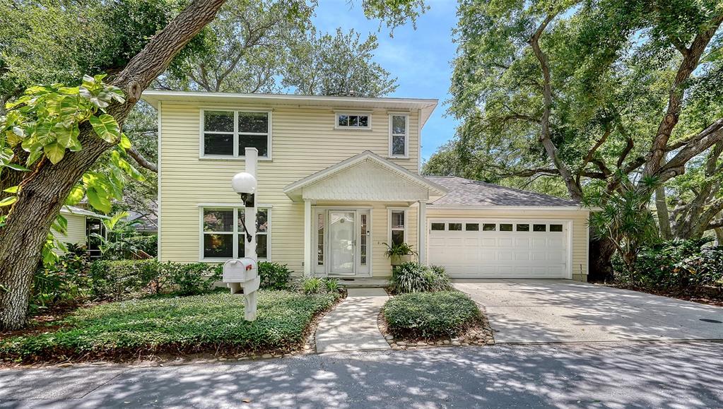 A two-story yellow house with a white garage and a front walkway under trees — 2304 63RD STREET COURT W, BRADENTON, FL