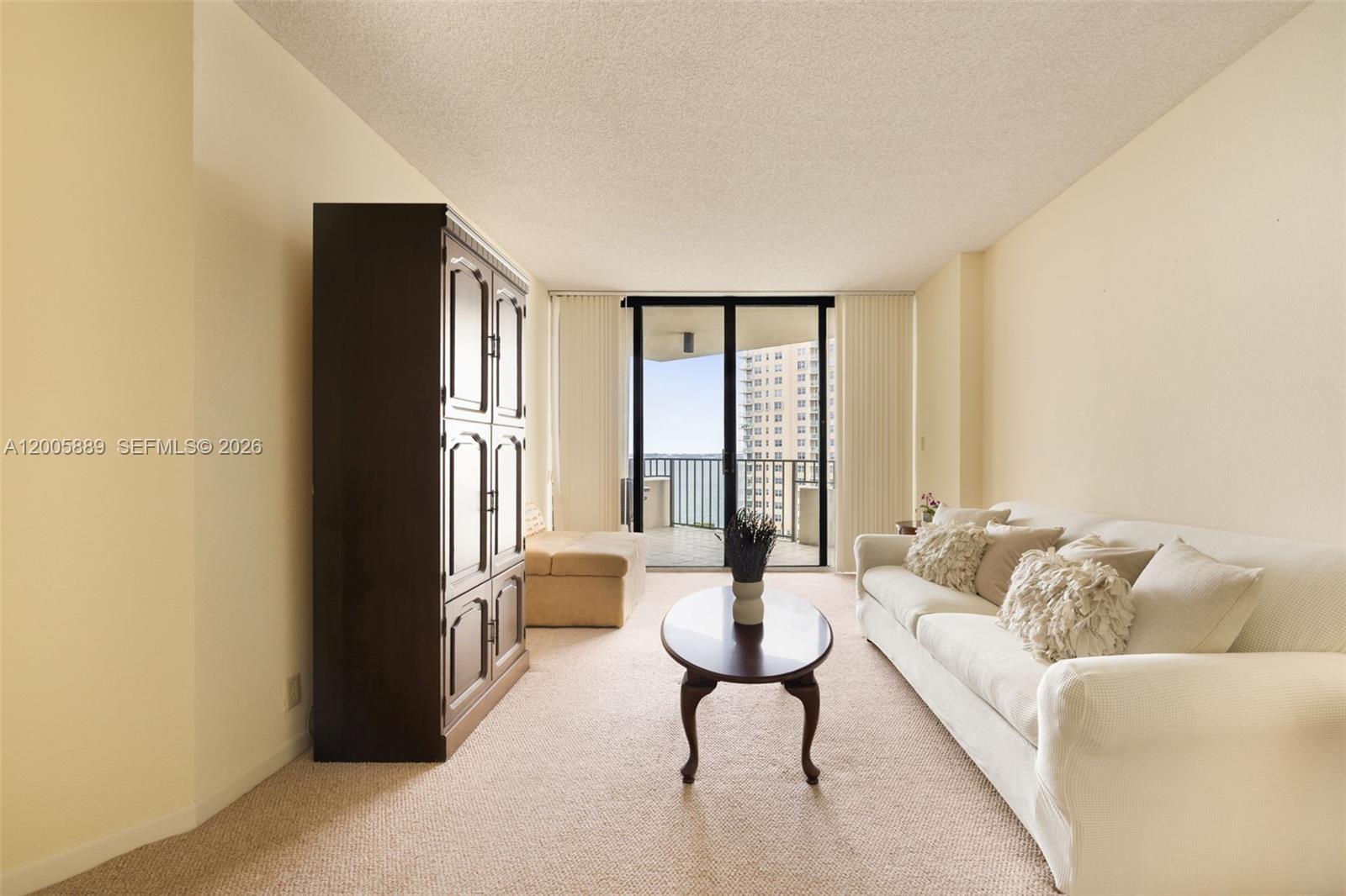 A living room features beige carpet, a white sofa, a dark cabinet, and a balcony view — 520 Brickell Key Dr # A1001, Miami FL 33131, MIAMI, FL