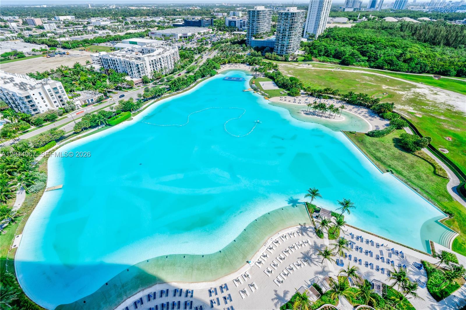An aerial view shows a large, turquoise man-made lagoon surrounded by sandy beaches and buildings — 2411 Laguna Circle # 1207, Miami FL 33181, MIAMI, FL
