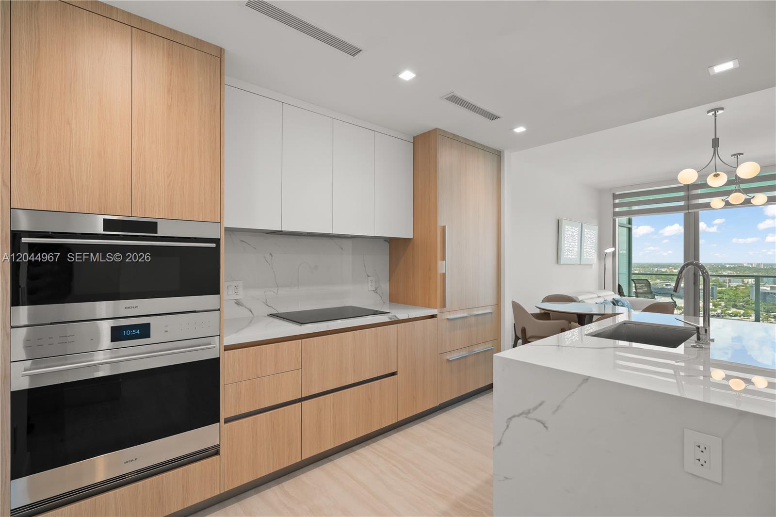 A modern kitchen features light wood cabinetry, white upper cabinets, marble countertops, and stainless appliances — 2411 Laguna Circle # 1207, Miami FL 33181, MIAMI, FL