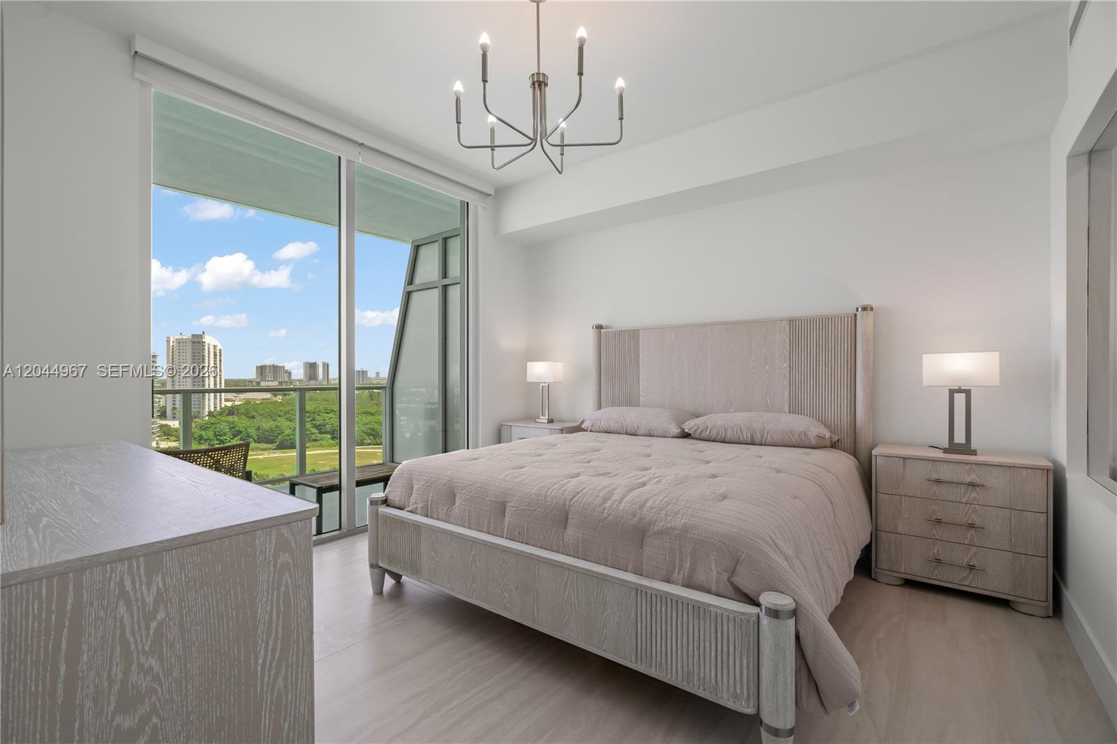 A bedroom features a light wood bed frame, matching nightstands, and a balcony with city views — 2411 Laguna Circle # 1207, Miami FL 33181, MIAMI, FL