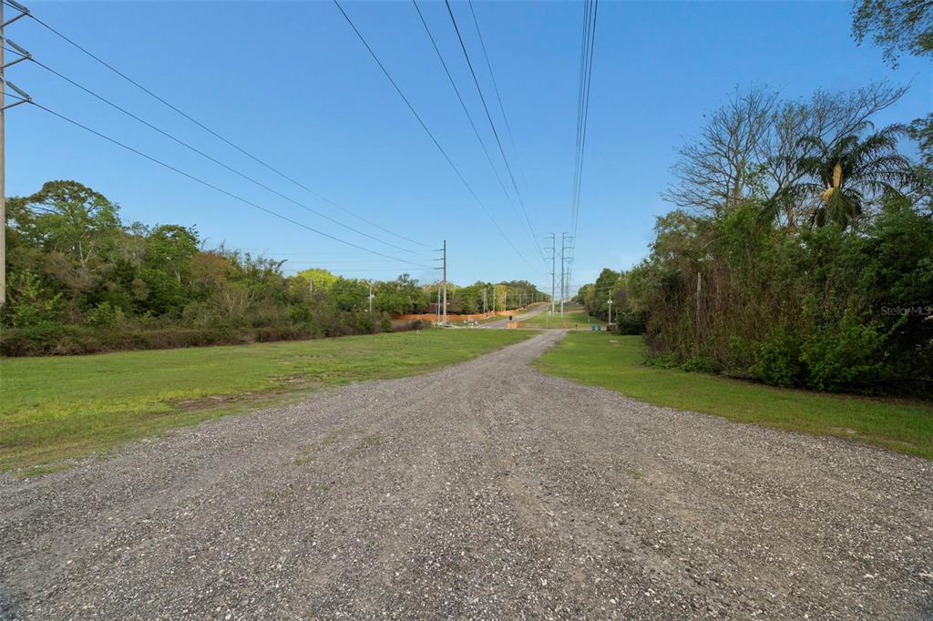 A gravel driveway leads through a grassy lot toward a road under power lines — 6890 COUNTY ROAD 95, PALM HARBOR, FL