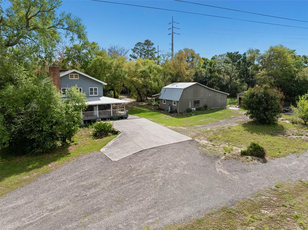 A two-story blue house with a porch stands next to a large metal workshop — 6890 COUNTY ROAD 95, PALM HARBOR, FL