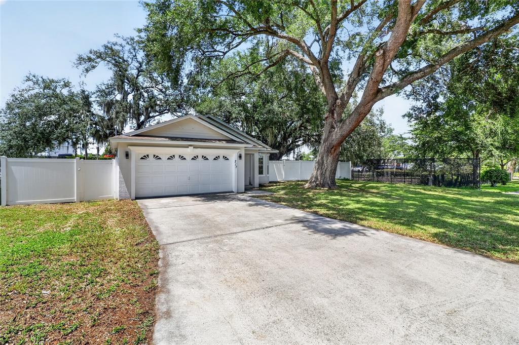 A concrete driveway leads to the garage of a single-story house with large oak trees — 217 E EDWARD STREET, LAKELAND, FL