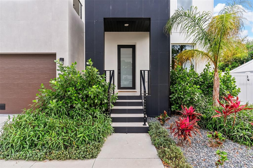 A modern house entrance features a black-framed door, concrete steps, and lush landscaping — 4604 W EUCLID AVENUE, TAMPA, FL