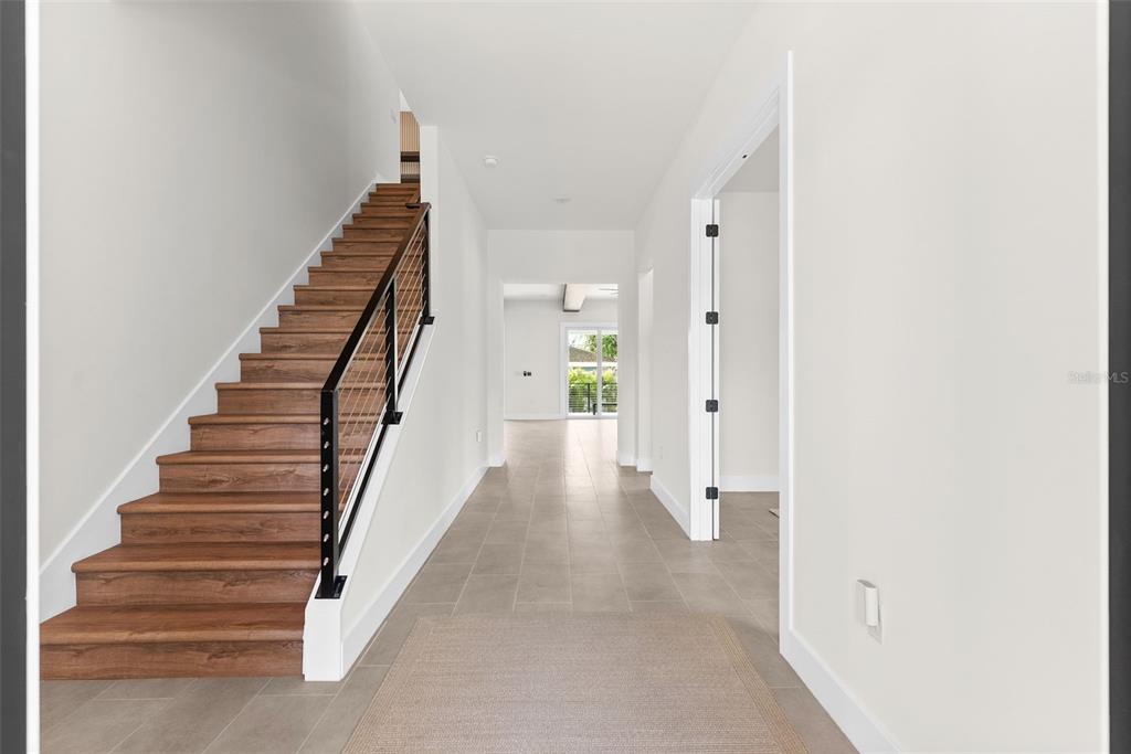 A bright hallway features a wood staircase with a black metal railing and tile flooring — 4604 W EUCLID AVENUE, TAMPA, FL