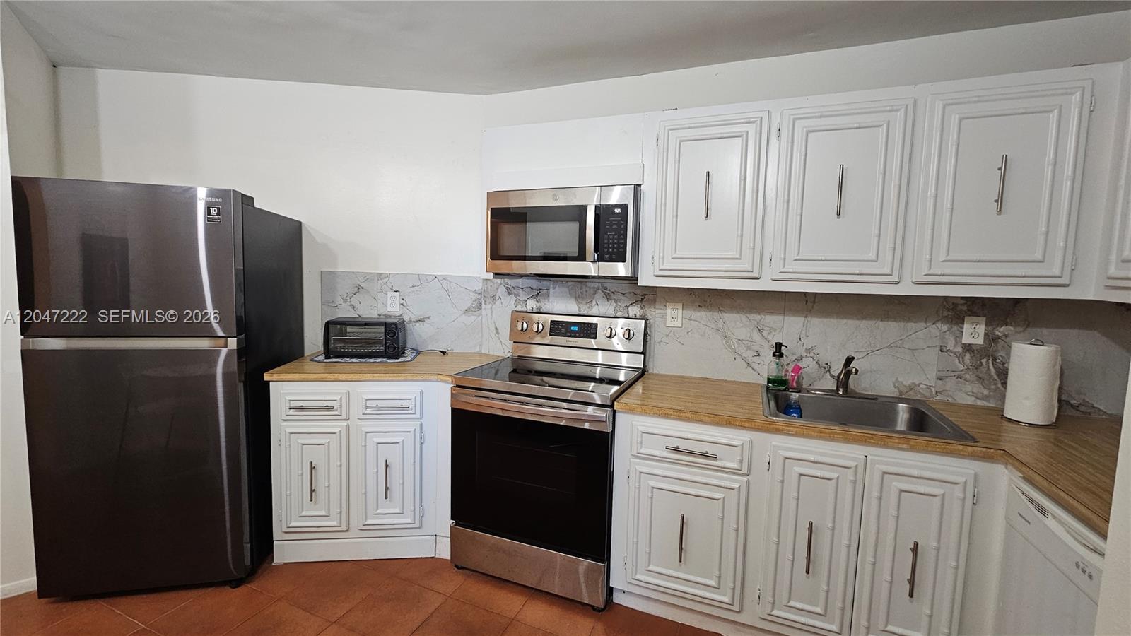A kitchen features white cabinets, stainless steel appliances, a marble-patterned backsplash, and wood-look countertops — 800 Parkview Dr # 912, Hallandale Beach FL 33009, HALLANDALE BEACH, FL