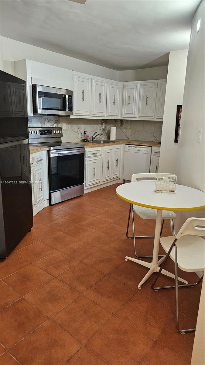 A kitchen features white cabinets, stainless steel appliances, a small round table, and tile flooring — 800 Parkview Dr # 912, Hallandale Beach FL 33009, HALLANDALE BEACH, FL