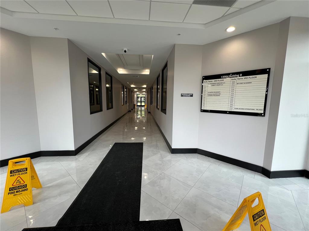 A bright office building hallway features white walls, tiled floors, and a directory sign — 13564 VILLAGE PARK DRIVE UNIT O-345, ORLANDO, FL