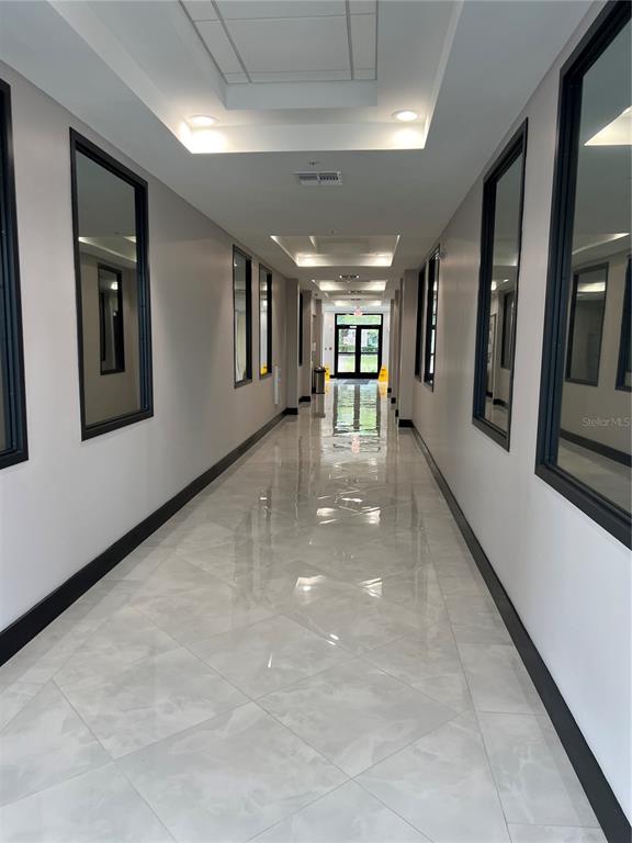 A long, brightly lit hallway features polished tile floors, dark-framed mirrors, and a glass-paned exit door — 13564 VILLAGE PARK DRIVE UNIT O-345, ORLANDO, FL