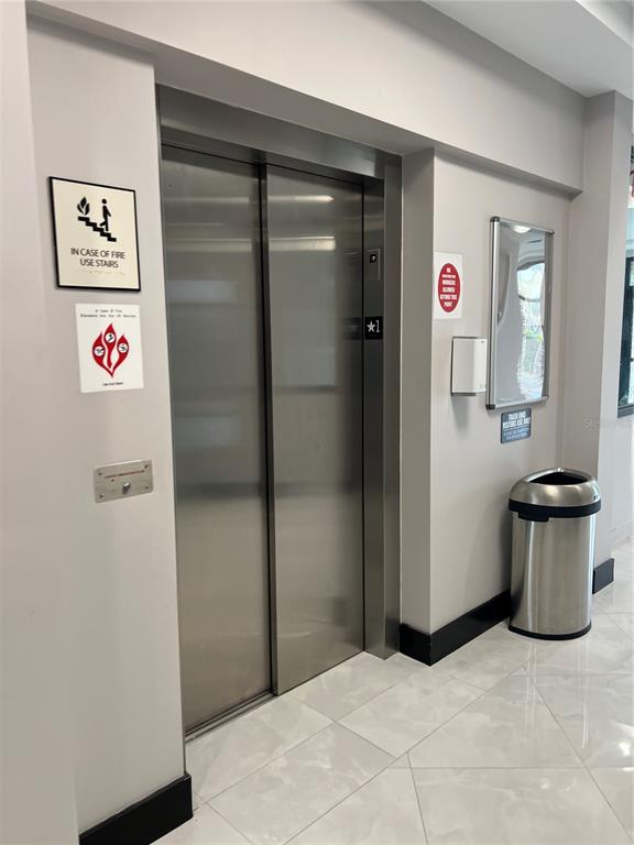 A stainless steel elevator sits in a hallway with light-colored tile floors and gray walls — 13564 VILLAGE PARK DRIVE UNIT O-345, ORLANDO, FL