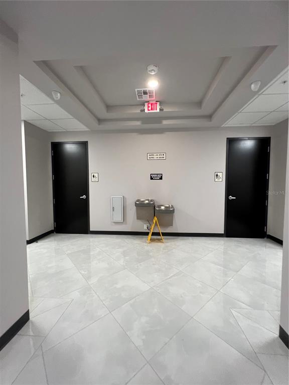 A hallway features two black doors, a water fountain, and light-colored tile flooring — 13564 VILLAGE PARK DRIVE UNIT O-345, ORLANDO, FL