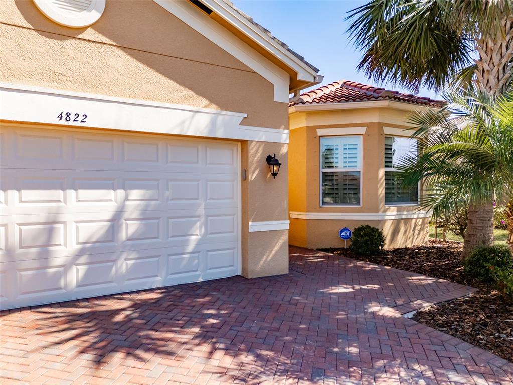A tan house exterior features a white garage door, a bay window, and paver driveway — 4822 GRAND BANKS DRIVE, WIMAUMA, FL