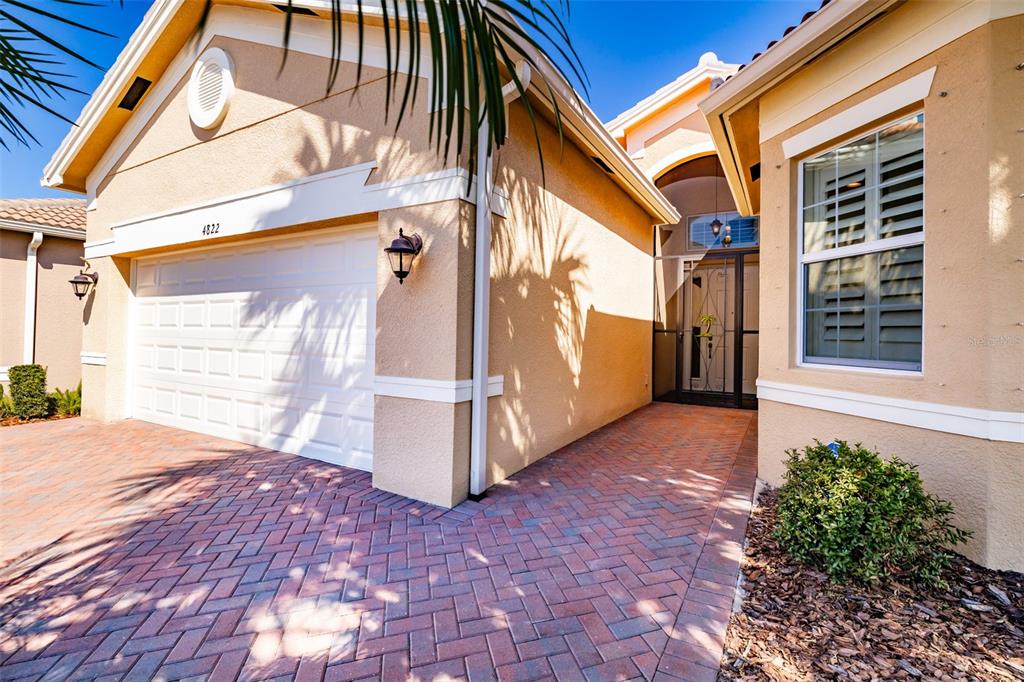 A beige house exterior features a white garage door, a brick driveway, and a front entrance — 4822 GRAND BANKS DRIVE, WIMAUMA, FL