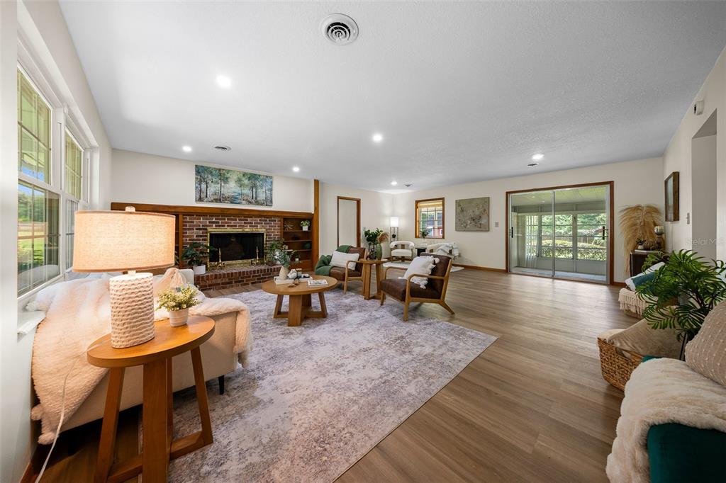 A spacious living room features a brick fireplace, wood-look flooring, and a sliding glass door — 130 SW 69TH STREET, OCALA, FL