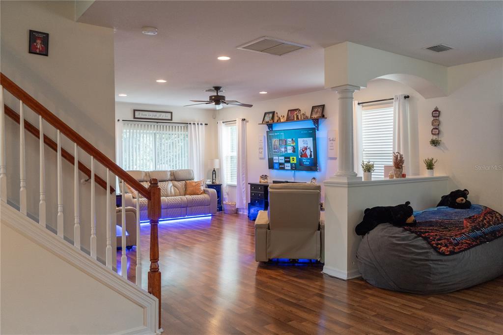 A living room features wood flooring, a staircase, a wall-mounted television, and a beanbag chair — 15647 GREYROCK DRIVE, SPRING HILL, FL