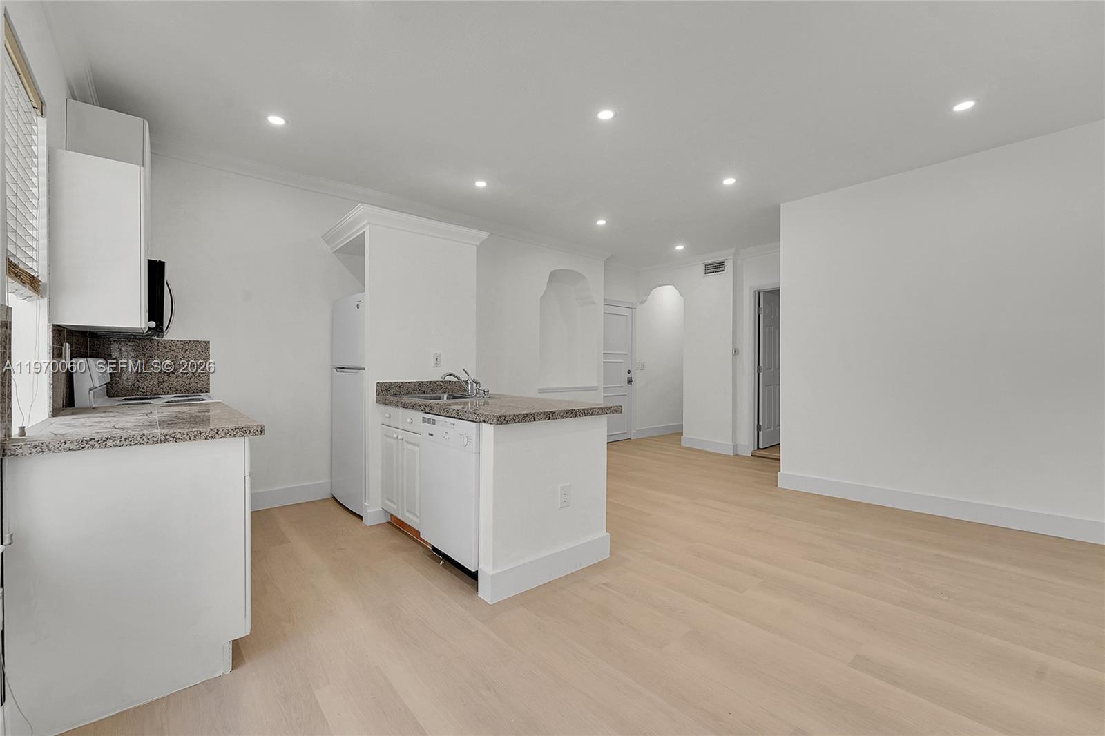 A kitchen with white cabinets, granite countertops, and light wood flooring opens to a living area — 1027 Pennsylvania Ave # 103, Miami Beach FL 33139, MIAMI BEACH, FL