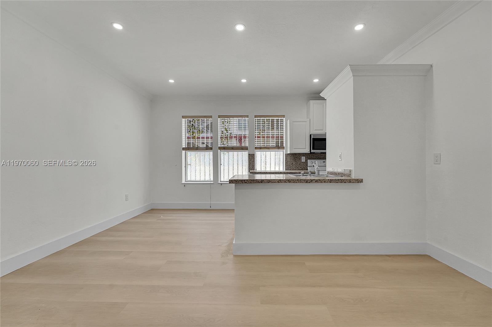 This room features light wood flooring, white walls, recessed lighting, and an open kitchen area — 1027 Pennsylvania Ave # 103, Miami Beach FL 33139, MIAMI BEACH, FL