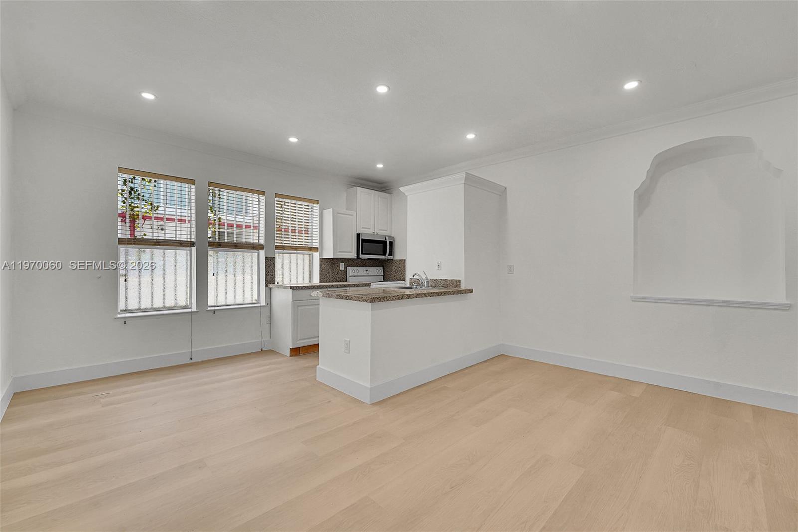 A kitchen with granite countertops and light wood flooring opens into a living area — 1027 Pennsylvania Ave # 103, Miami Beach FL 33139, MIAMI BEACH, FL