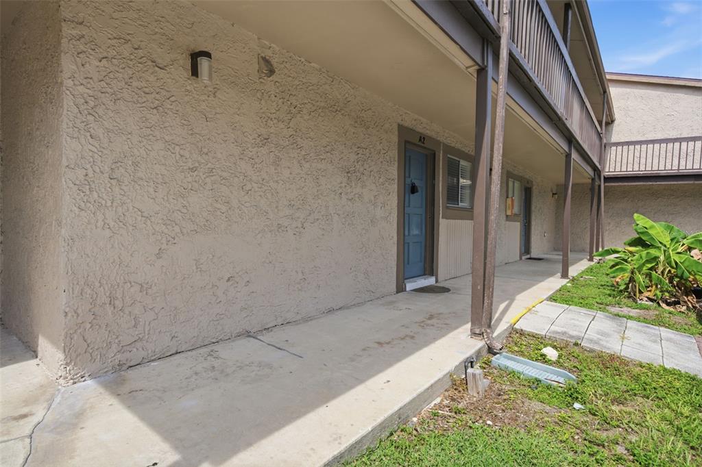 An exterior view of a ground-level apartment entrance with a concrete walkway and stucco walls — 6314 NEWTOWN CIRCLE UNIT 14A2, TAMPA, FL