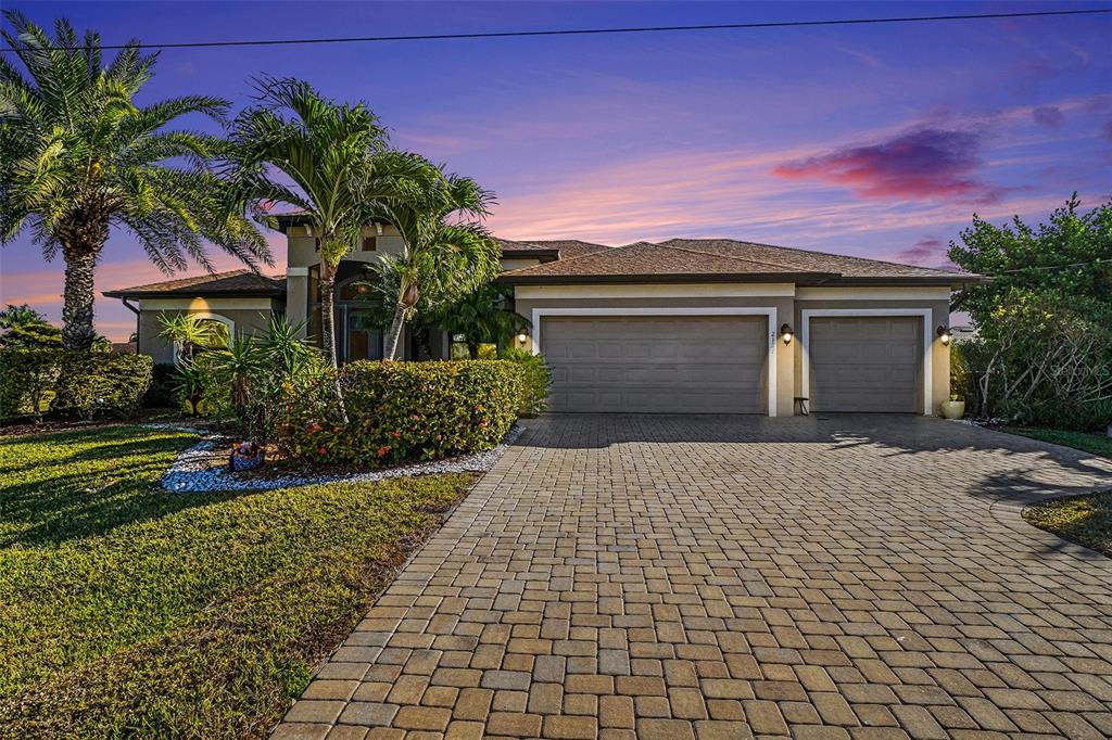 A single-story house with a paved driveway, a three-car garage, and palm trees at sunset — 2127 SE 17TH PLACE, CAPE CORAL, FL