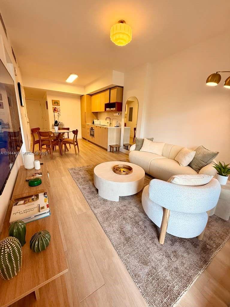 A living room and kitchen area with light wood floors, neutral furniture, and modern decor — 90 NE 32 # 302, Miami FL 33137, MIAMI, FL