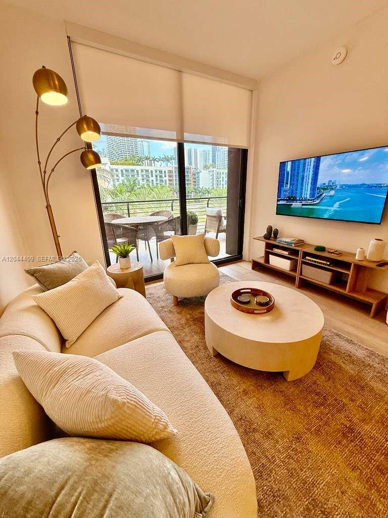 A modern living room features a curved sofa, round coffee table, and a balcony view — 90 NE 32 # 302, Miami FL 33137, MIAMI, FL