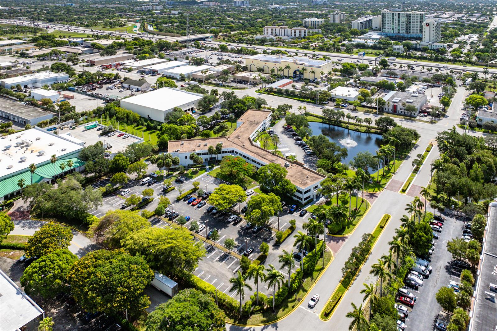 An aerial view shows a multi-story office building with a parking lot and a pond — 555 SW 12th Avenue # 106, Pompano Beach FL 33069, POMPANO BEACH, FL