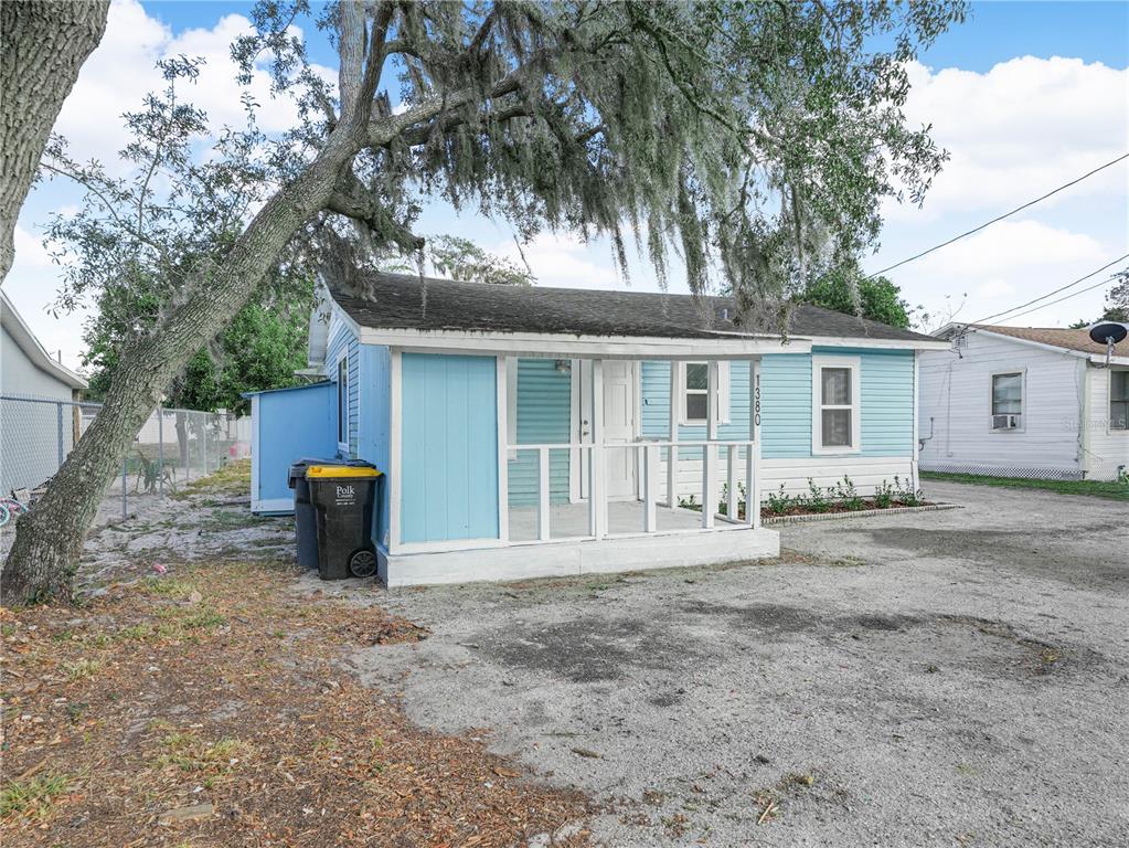 A light blue single-story house features a screened-in front porch and a gravel driveway — 1380 35TH STREET NW, WINTER HAVEN, FL