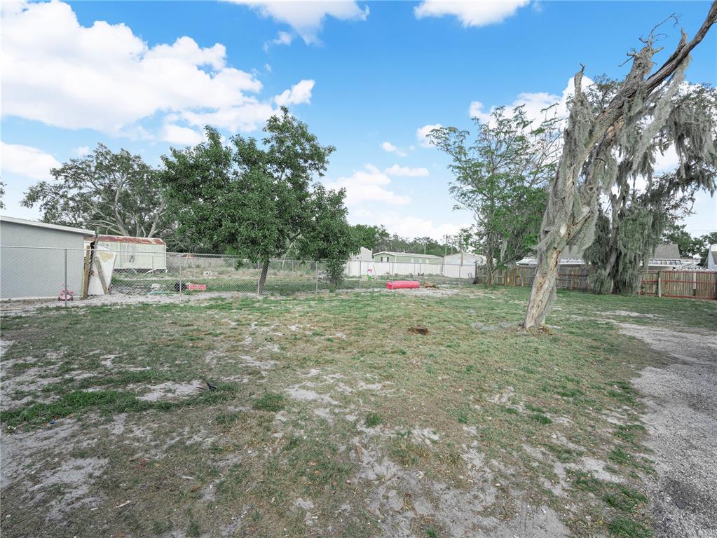 A grassy backyard features a chain-link fence, a large tree with Spanish moss, and outbuildings — 1380 35TH STREET NW, WINTER HAVEN, FL