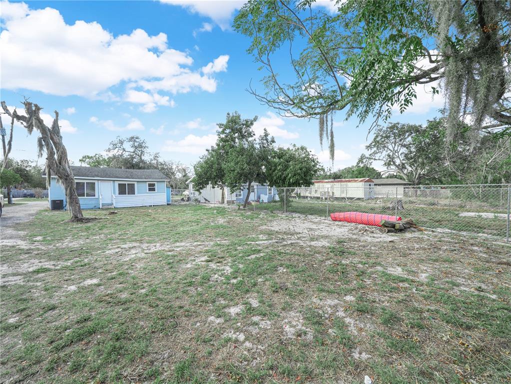 A grassy backyard features a light blue house, a chain-link fence, and mature trees — 1380 35TH STREET NW, WINTER HAVEN, FL