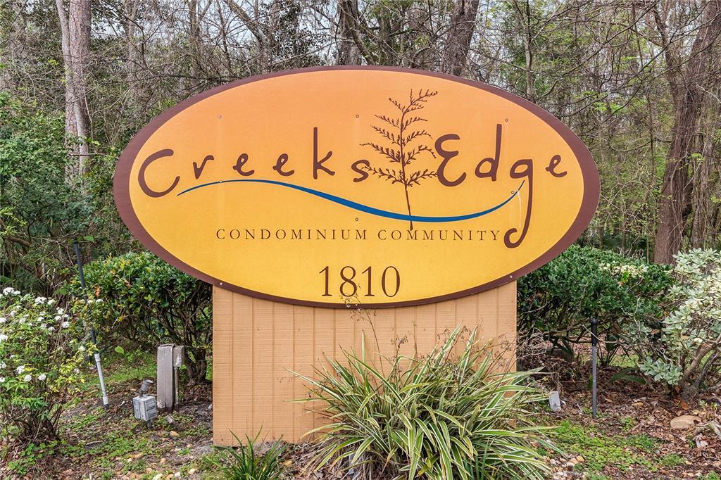 An oval sign for Creeks Edge Condominium Community stands in a wooded area — 1810 NW 23RD BOULEVARD UNIT 174, GAINESVILLE, FL