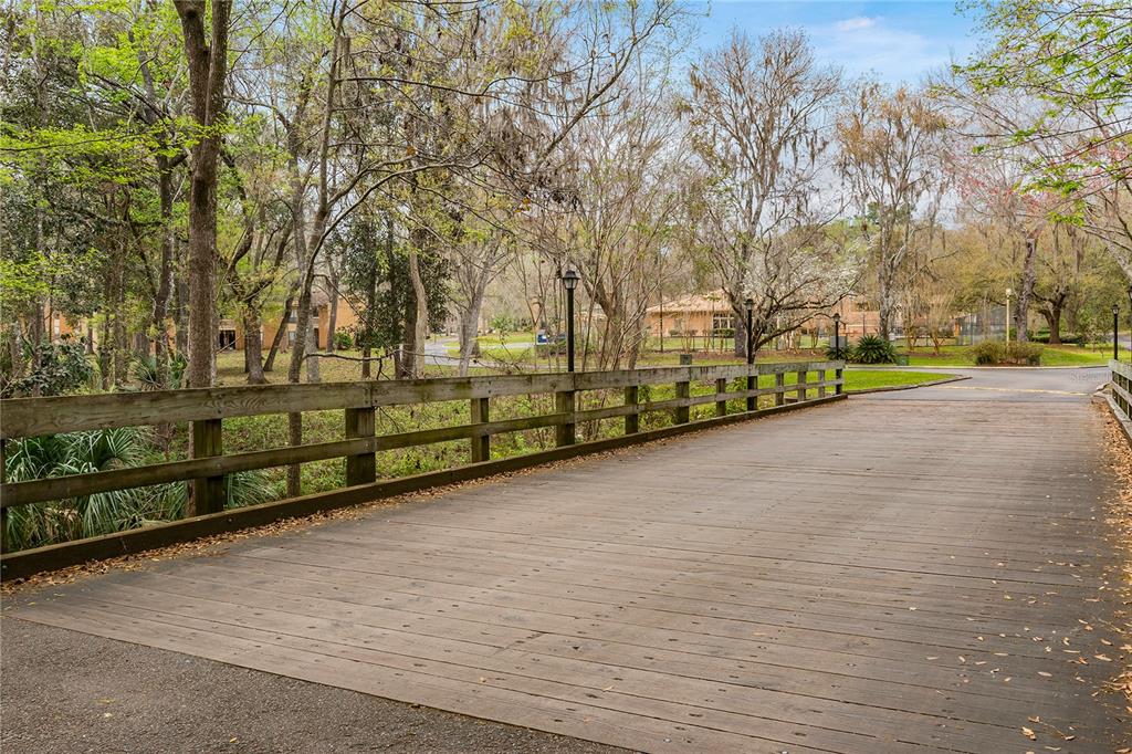 A wooden bridge with railings leads toward a residential complex surrounded by trees — 1810 NW 23RD BOULEVARD UNIT 174, GAINESVILLE, FL